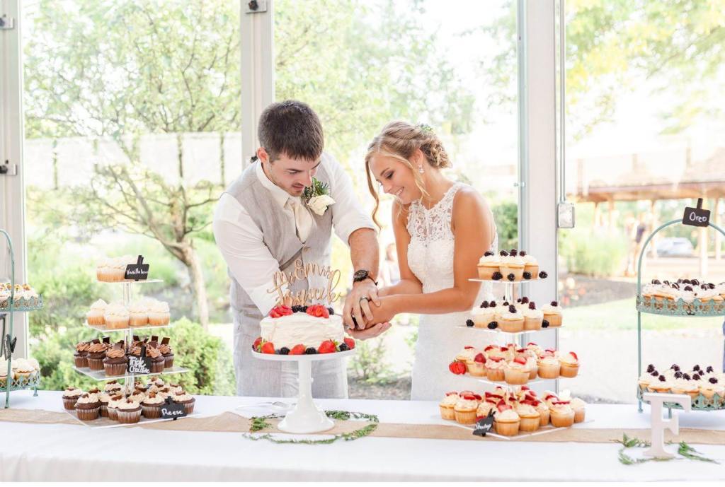 Kaylee and Nate cutting into white cake with flowers on wedding dessert banquet table